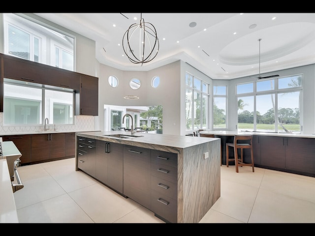 12990 Marsh Lndg, Palm Beach Gardens, FL 33418 - kitchen featuring modern cabinets, a tray ceiling, light tile patterned floors, tasteful backsplash, and an island with sink