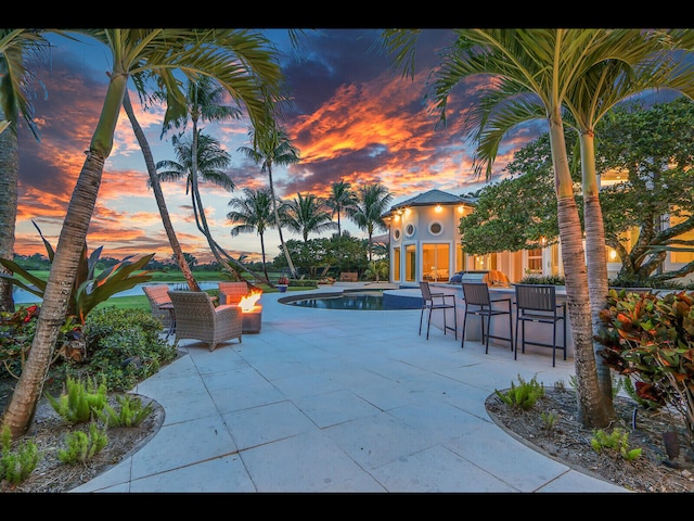 12990 Marsh Lndg, Palm Beach Gardens, FL 33418 - patio terrace at dusk with a patio area, an outdoor fire pit, an outdoor pool, and exterior bar