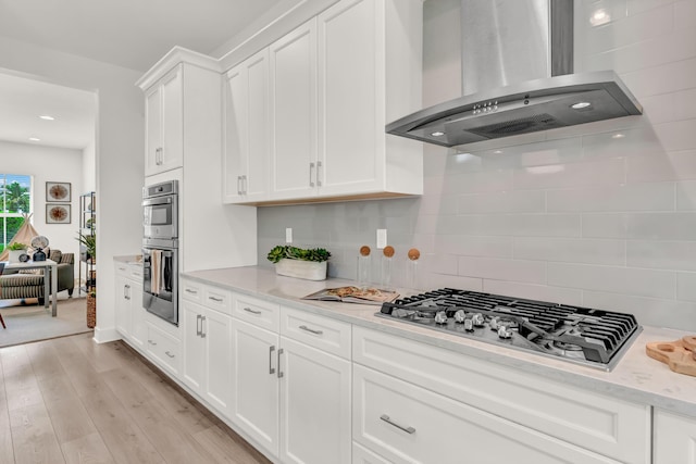 13330 Machiavelli Way, Palm Beach Gardens, FL 33418 - kitchen featuring wall chimney range hood, appliances with stainless steel finishes, white cabinetry, tasteful backsplash, and light wood finished floors