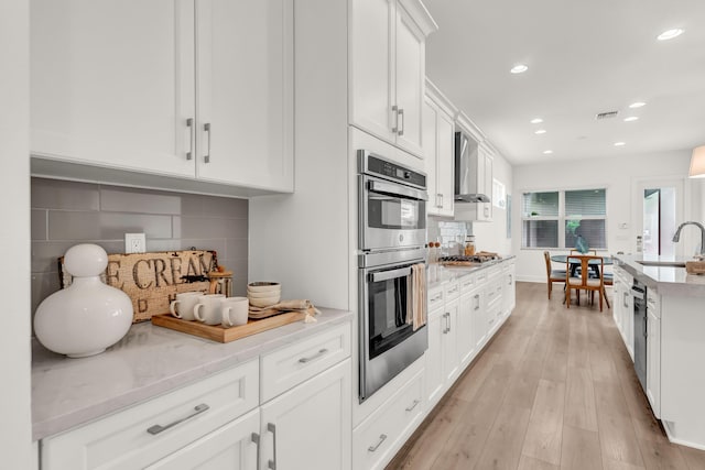 13330 Machiavelli Way, Palm Beach Gardens, FL 33418 - kitchen with stainless steel appliances, wall chimney range hood, a sink, white cabinetry, and recessed lighting