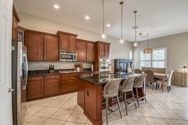 10295 SW Waterway Ln, Port Saint Lucie, FL 34987 - kitchen with stainless steel appliances, decorative backsplash, an island with sink, dark stone counters, and hanging light fixtures