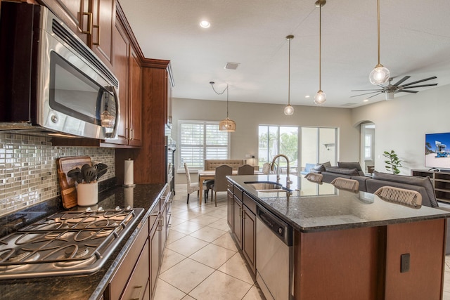 10295 SW Waterway Ln, Port Saint Lucie, FL 34987 - kitchen with appliances with stainless steel finishes, decorative backsplash, a center island with sink, dark stone counters, and hanging light fixtures