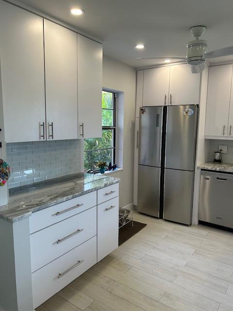 100 Lake Terry Dr, West Palm Beach, FL 33411 - kitchen featuring stainless steel appliances, light stone countertops, white cabinetry, decorative backsplash, and light wood finished floors