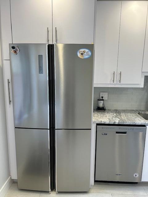 100 Lake Terry Dr, West Palm Beach, FL 33411 - kitchen featuring appliances with stainless steel finishes, white cabinetry, light stone countertops, and backsplash