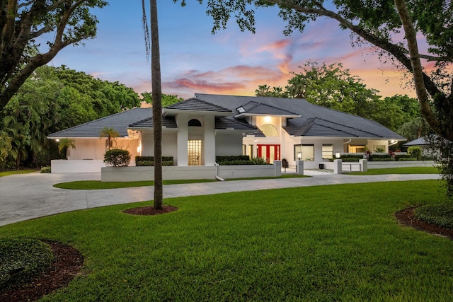 8076 Twin Lake Dr, Boca Raton, FL 33496 - back of property at dusk featuring curved driveway, a lawn, and stucco siding