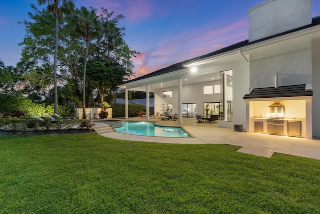 8076 Twin Lake Dr, Boca Raton, FL 33496 - back of house at dusk featuring exterior kitchen, a lawn, a patio, and stucco siding