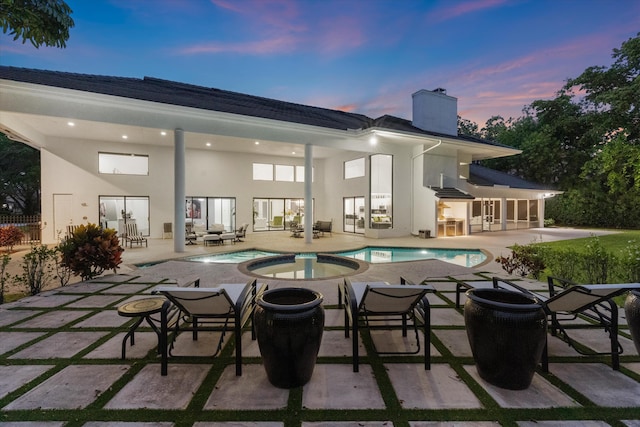 8076 Twin Lake Dr, Boca Raton, FL 33496 - back of house at dusk featuring a chimney, a patio, stucco siding, a pool with connected hot tub, and french doors