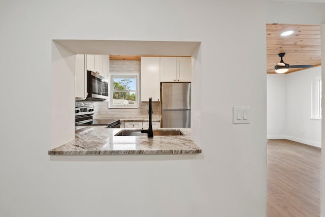 677 NE Alice St, Jensen Beach, FL 34957 - kitchen featuring appliances with stainless steel finishes, a sink, backsplash, light stone countertops, and wood finished floors