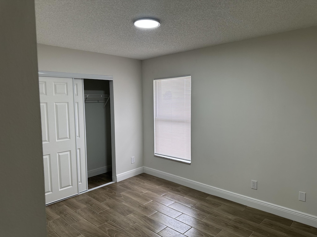 496 E Jordan Blvd, Pahokee, FL 33476 - unfurnished bedroom featuring wood finish floors, a textured ceiling, baseboards, and a closet