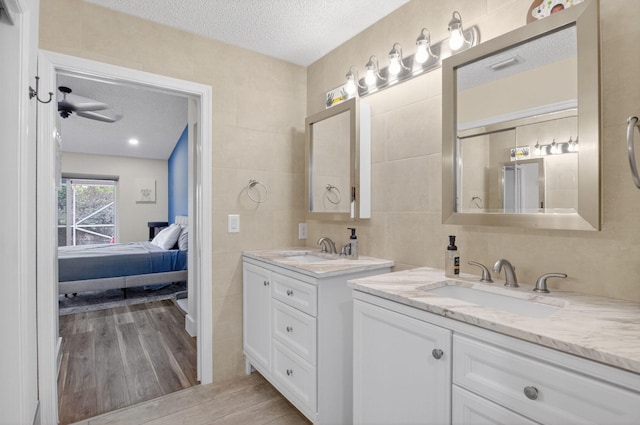 11080 Lakeaire Cir, Boca Raton, FL 33498 - ensuite bathroom featuring a textured ceiling, tile walls, wood finished floors, and two vanities