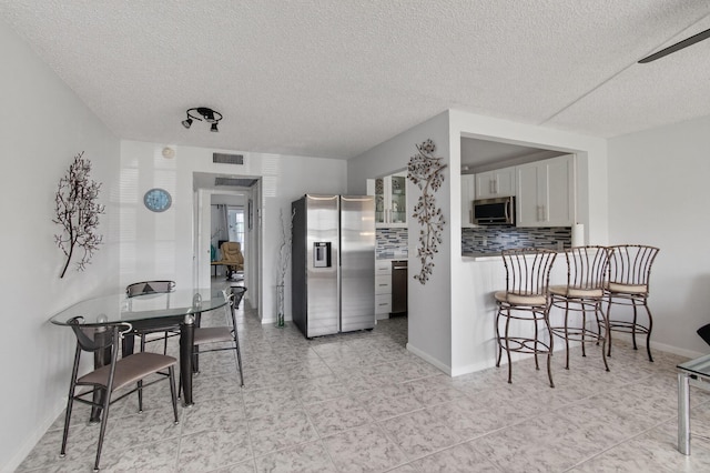 1116 Cambridge E Unit E, Deerfield Beach, FL 33442 - kitchen with appliances with stainless steel finishes, a textured ceiling, decorative backsplash, a breakfast bar area, and white cabinets