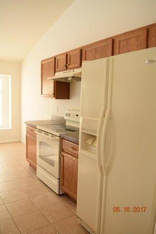 1701 SW Victor Ln SW, Port Saint Lucie, FL 34984 - kitchen featuring white appliances, vaulted ceiling, under cabinet range hood, brown cabinets, and baseboards