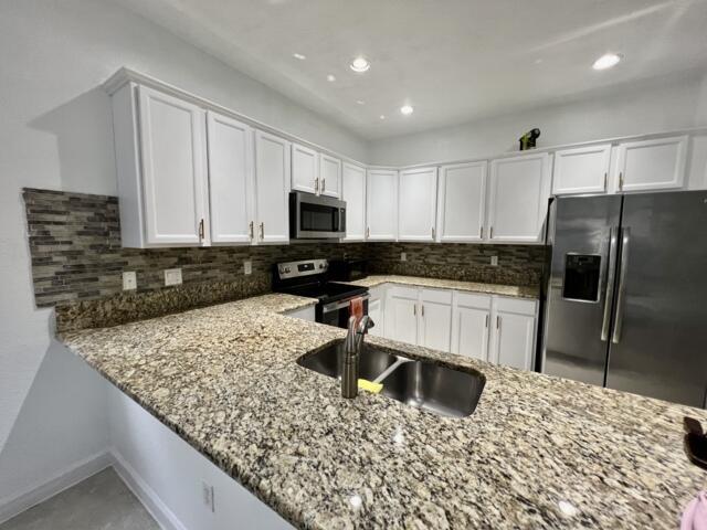 3841 E Aspen Leaf Dr, Boynton Beach, FL 33436 - kitchen featuring appliances with stainless steel finishes, light stone countertops, a sink, white cabinets, and decorative backsplash