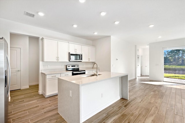 18478 Claybrook St, Jupiter, FL 33458 - kitchen featuring stainless steel appliances, a sink, light wood-style floors, a kitchen island with sink, and light countertops