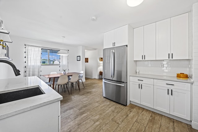 407 Riverside Dr, Palm Beach Gardens, FL 33410 - kitchen featuring freestanding refrigerator, light wood-type flooring, white cabinetry, tasteful backsplash, and light stone counters