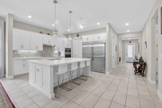 4652 Saxon Rd, Coconut Creek, FL 33073 - kitchen featuring appliances with stainless steel finishes, under cabinet range hood, white cabinets, an island with sink, and recessed lighting