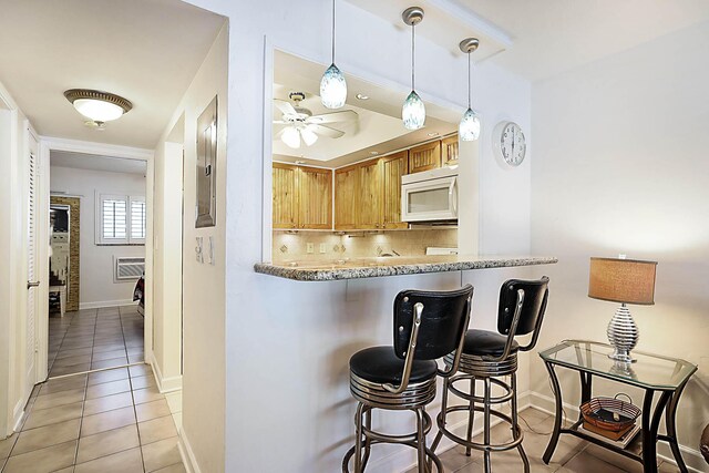 2501 N Ocean Blvd Unit 3, Pompano Beach, FL 33062 - kitchen with white microwave, light tile patterned floors, decorative backsplash, a ceiling fan, and a breakfast bar