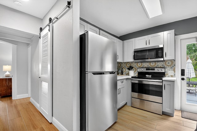 404 S M St Unit 1, Lake Worth Beach, FL 33460 - kitchen featuring stainless steel appliances, a barn door, light wood-type flooring, light countertops, and backsplash