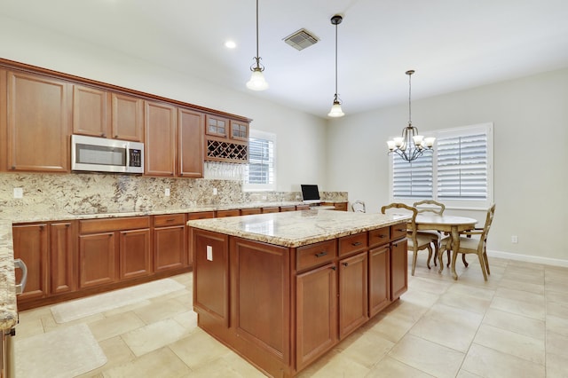 5621 SW Longspur Ln, Palm City, FL 34990 - kitchen featuring stainless steel microwave, decorative backsplash, light stone counters, and hanging light fixtures