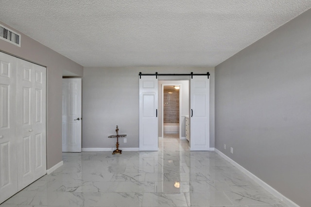 5500 NW 2nd Ave Three, Unit Three, Boca Raton, FL 33487 - unfurnished bedroom with a barn door, baseboards, light marble finish floors, a textured ceiling, and ensuite bathroom