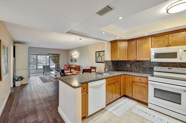 2901 NW 46th Ave Unit 101, Lauderdale Lakes, FL 33313 - kitchen with white appliances, a peninsula, a raised ceiling, dark stone countertops, and decorative backsplash