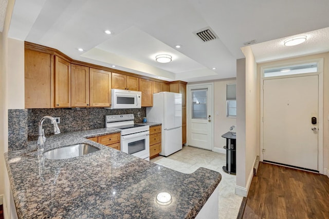 2901 NW 46th Ave Unit 101, Lauderdale Lakes, FL 33313 - kitchen featuring white appliances, a raised ceiling, tasteful backsplash, dark stone counters, and brown cabinetry