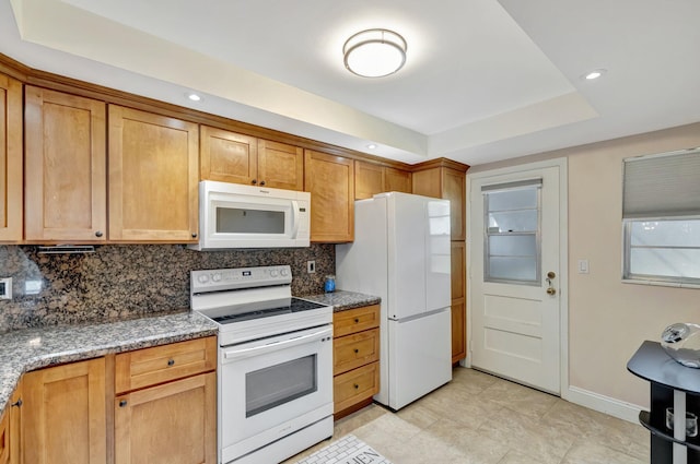 2901 NW 46th Ave Unit 101, Lauderdale Lakes, FL 33313 - kitchen featuring white appliances, decorative backsplash, a tray ceiling, brown cabinetry, and dark stone countertops