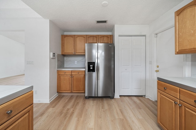 17832 43rd Rd N, Loxahatchee, FL 33470 - kitchen featuring stainless steel fridge, light wood-style floors, brown cabinets, a textured ceiling, and light countertops