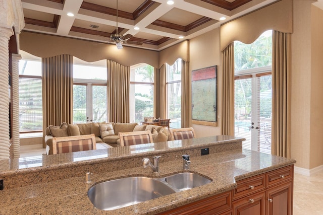 123 Grand Palm Way, Palm Beach Gardens, FL 33418 - kitchen with a sink, light stone countertops, beamed ceiling, brown cabinets, and french doors