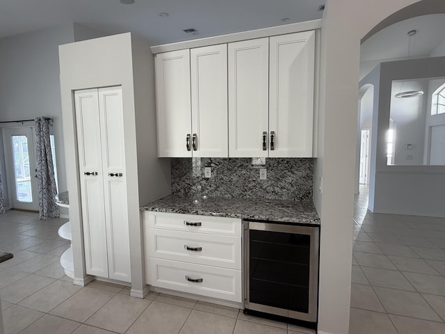 9360 Cove Point Cir, Boynton Beach, FL 33472 - kitchen with wine cooler, arched walkways, light tile patterned floors, dark stone counters, and decorative backsplash