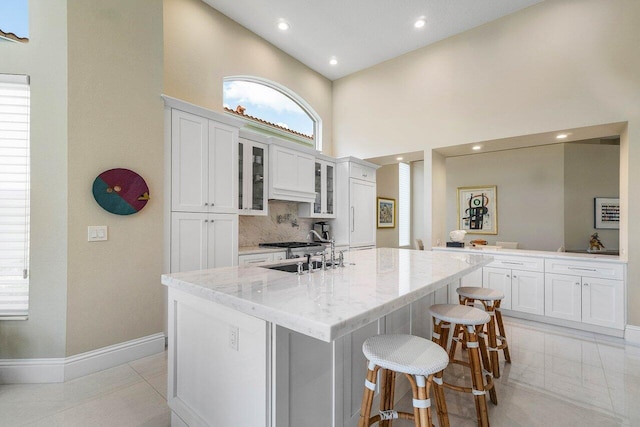 391 Isle Ct, Palm Beach Gardens, FL 33418 - kitchen with a high ceiling, glass insert cabinets, a center island with sink, a breakfast bar area, and white cabinetry