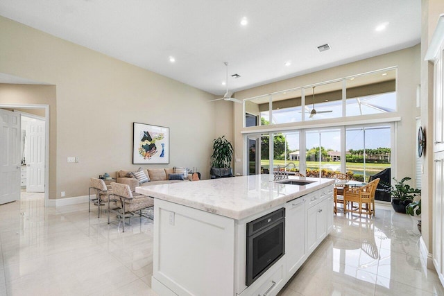 391 Isle Ct, Palm Beach Gardens, FL 33418 - kitchen featuring ceiling fan, light stone counters, recessed lighting, white cabinets, and an island with sink