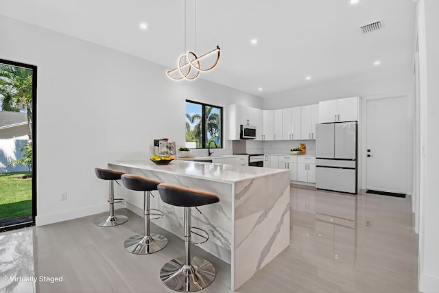 3920 Espan Ct, Palm Springs, FL 33461 - kitchen with freestanding refrigerator, a peninsula, a breakfast bar area, white cabinetry, and stainless steel microwave