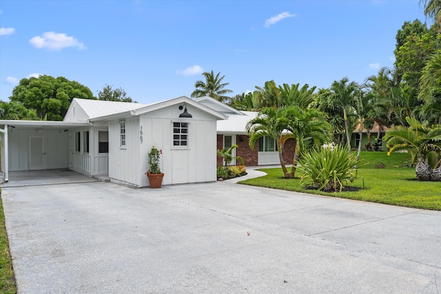 1567 NE Sottong Ave, Jensen Beach, FL 34957 - view of front facade with board and batten siding, concrete driveway, a front yard, and an attached carport