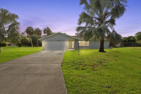 1830 Well Rd, Fort Pierce, FL 34945 - ranch-style house featuring an attached garage, driveway, a front lawn, and stucco siding