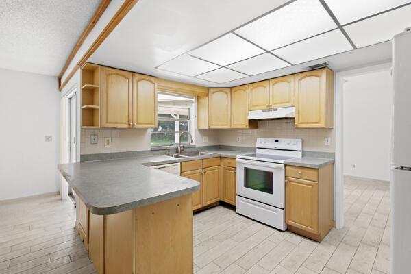 1830 Well Rd, Fort Pierce, FL 34945 - kitchen with white appliances, under cabinet range hood, light brown cabinetry, a sink, and a peninsula