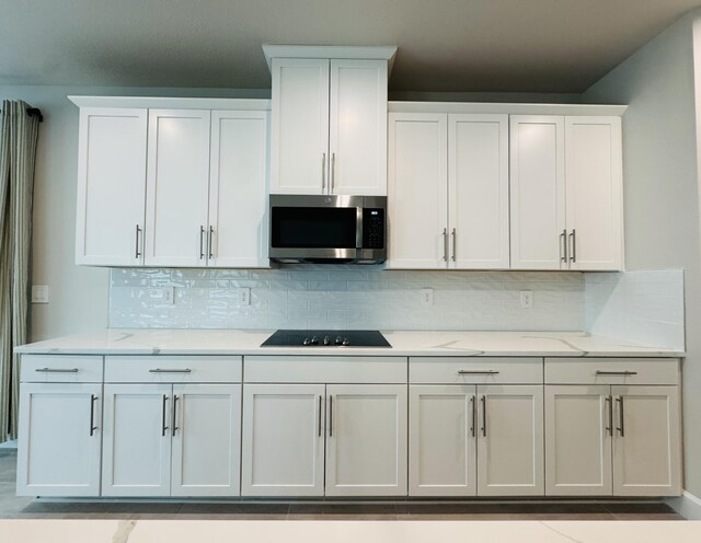 163 SW Pomeroy St, Stuart, FL 34997 - kitchen featuring stainless steel microwave, black electric cooktop, backsplash, and white cabinetry