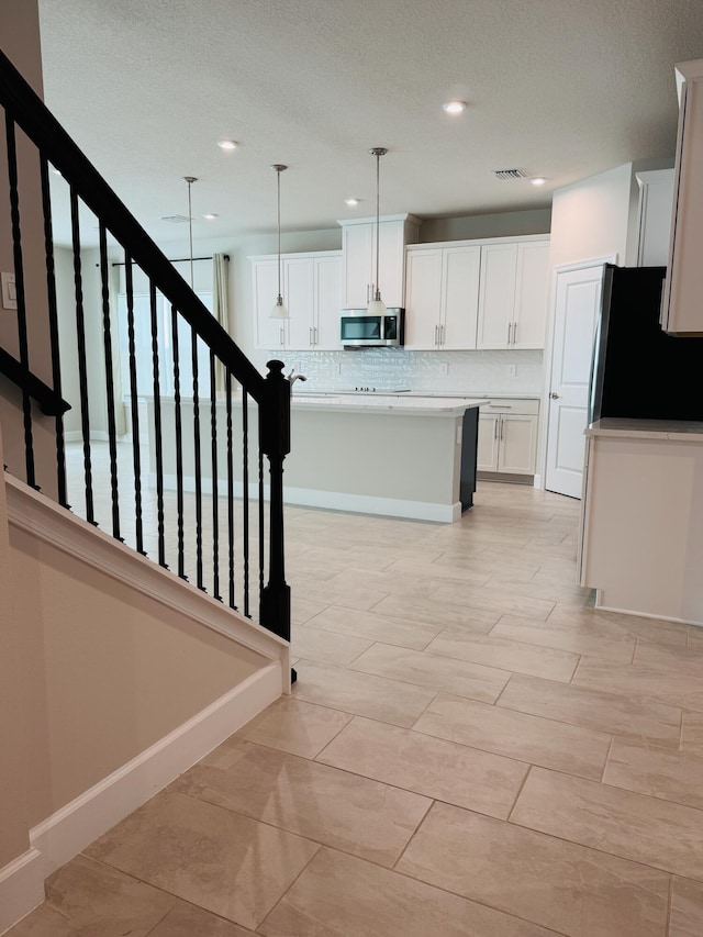163 SW Pomeroy St, Stuart, FL 34997 - kitchen featuring freestanding refrigerator, stainless steel microwave, tasteful backsplash, white cabinets, and recessed lighting