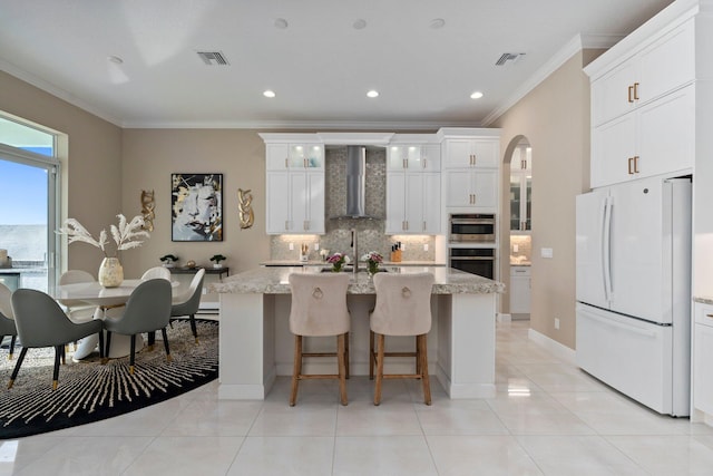 8650 SW Felicita Way, Port Saint Lucie, FL 34987 - kitchen featuring freestanding refrigerator, wall chimney exhaust hood, ornamental molding, an island with sink, and backsplash