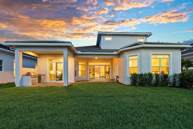 8650 SW Felicita Way, Port Saint Lucie, FL 34987 - back of property at dusk featuring exterior kitchen, a yard, and stucco siding