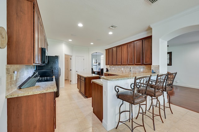 5857 NW Leghorn Ave, Port Saint Lucie, FL 34986 - kitchen featuring crown molding, a center island, arched walkways, light stone countertops, and decorative backsplash