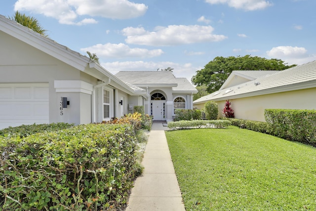 1365 Wilderness Rd, West Palm Beach, FL 33409 - property entrance with a yard, stucco siding, and a garage