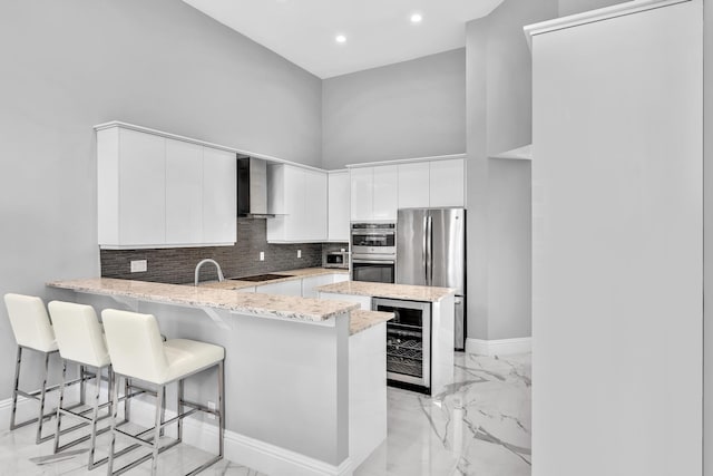20677 NW 26th Ct, Boca Raton, FL 33434 - kitchen with wine cooler, stainless steel appliances, wall chimney range hood, a peninsula, and a towering ceiling