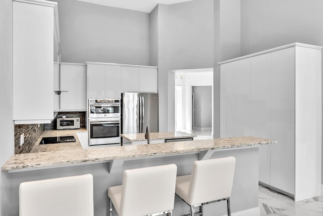 20677 NW 26th Ct, Boca Raton, FL 33434 - kitchen featuring stainless steel appliances, a peninsula, decorative backsplash, light stone counters, and light marble finish floors