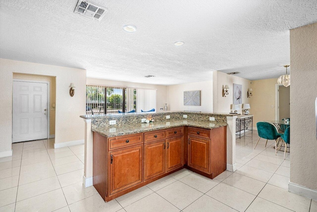 1209 N Australian Ave, West Palm Beach, FL 33401 - kitchen with a textured ceiling, brown cabinets, light stone countertops, light tile patterned floors, and a center island