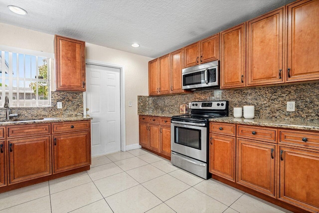1209 N Australian Ave, West Palm Beach, FL 33401 - kitchen with appliances with stainless steel finishes, brown cabinetry, light tile patterned floors, light stone counters, and a textured ceiling