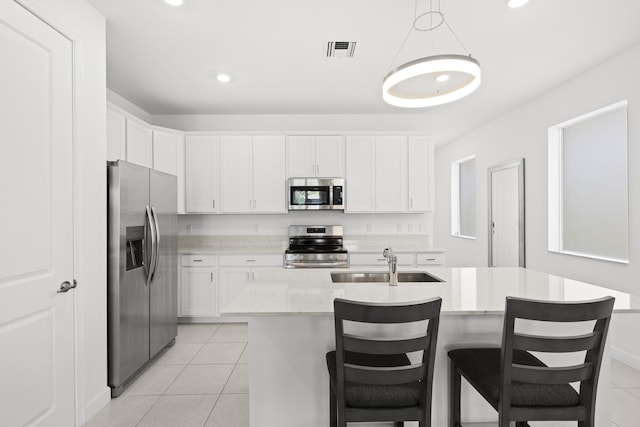 5697 Graceful Way, Delray Beach, FL 33484 - kitchen with stainless steel appliances, light tile patterned floors, white cabinetry, decorative light fixtures, and a center island with sink