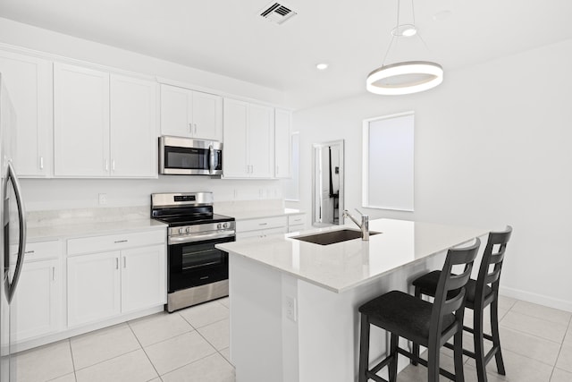 5697 Graceful Way, Delray Beach, FL 33484 - kitchen featuring appliances with stainless steel finishes, light tile patterned flooring, white cabinetry, a kitchen island with sink, and decorative light fixtures