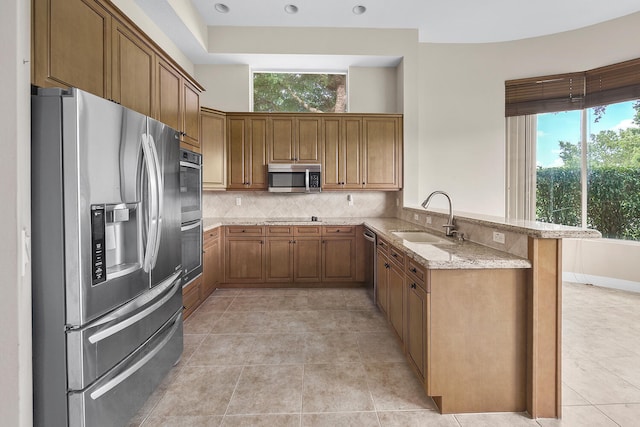 9724 Via Grandezza, Wellington, FL 33411 - kitchen with appliances with stainless steel finishes, brown cabinetry, light stone countertops, a peninsula, and decorative backsplash