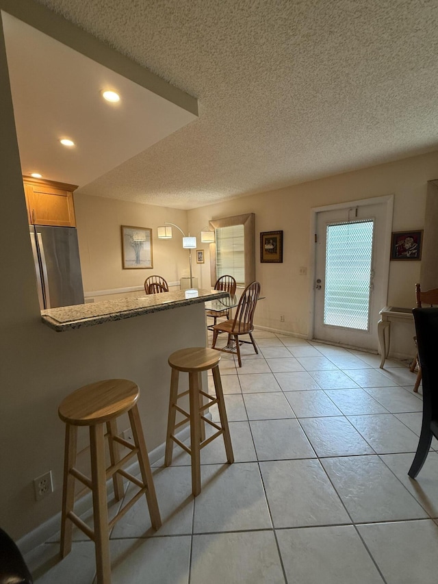 1046 Wolverton C, Boca Raton, FL 33434 - kitchen with freestanding refrigerator, a textured ceiling, a kitchen bar, recessed lighting, and a peninsula
